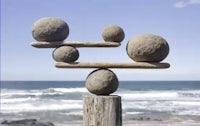 three balancing spheres on a wooden post in front of the ocean