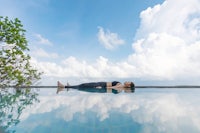 a woman laying on top of a pool with clouds in the background